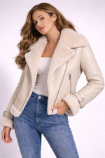 Woman wearing a beige shearling jacket and blue jeans on a white background